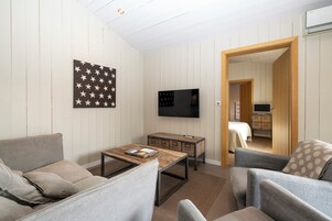 Un salon moderne comprenant un canapé, un fauteuil, une table basse et un téléviseur à écran plat fixé au mur. On y trouve également un meuble en bois avec des tiroirs et une petite table avec un plateau.