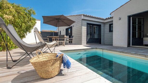 Un espace piscine extérieur moderne, doté d’une terrasse en bois, de chaises longues et d’un coin salon abrité.
