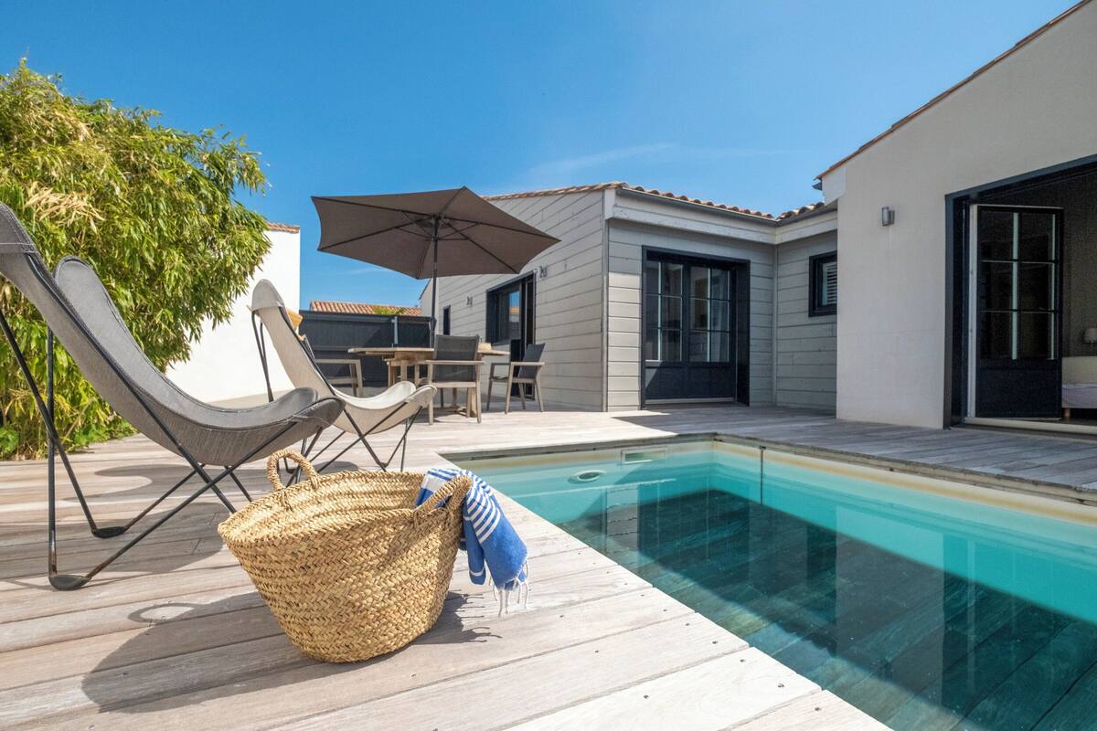 Un espace piscine extérieur moderne, doté d’une terrasse en bois, de chaises longues et d’un coin salon abrité.