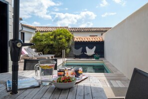 A poolside table with a bowl of watermelon and drinks, a patio umbrella, and a pool in the background. - Mv Lodge (La Couarde-sur-Mer)