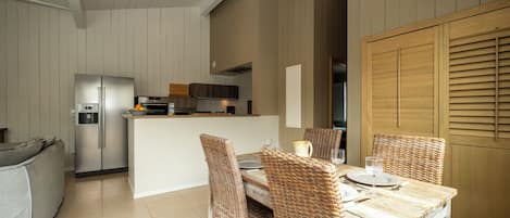 Una cocina moderna con una isla central, armarios blancos y un comedor con sillas de mimbre y una mesa de madera.