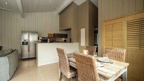 Une cuisine moderne dotée d’un îlot central, de meubles blancs et d’un coin repas avec des chaises en osier et une table en bois.