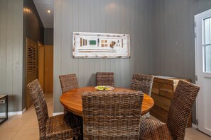 A dining area with a round wooden table surrounded by wicker chairs, a rustic wall art piece above, and a wooden cabinet to the right. - Mv Lodge (La Couarde-sur-Mer)