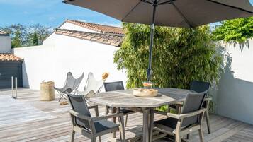 An outdoor patio with a wooden table and chairs, a large umbrella, and a basket of bread.