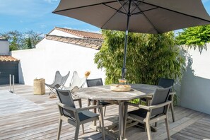 An outdoor patio with a wooden table and chairs, a large umbrella, and a basket of bread. - Mv Lodge (La Couarde-sur-Mer)