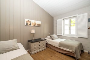 Ett sovrum med två sängar, en byrå, en lampa och ett fönster med fönsterluckor.