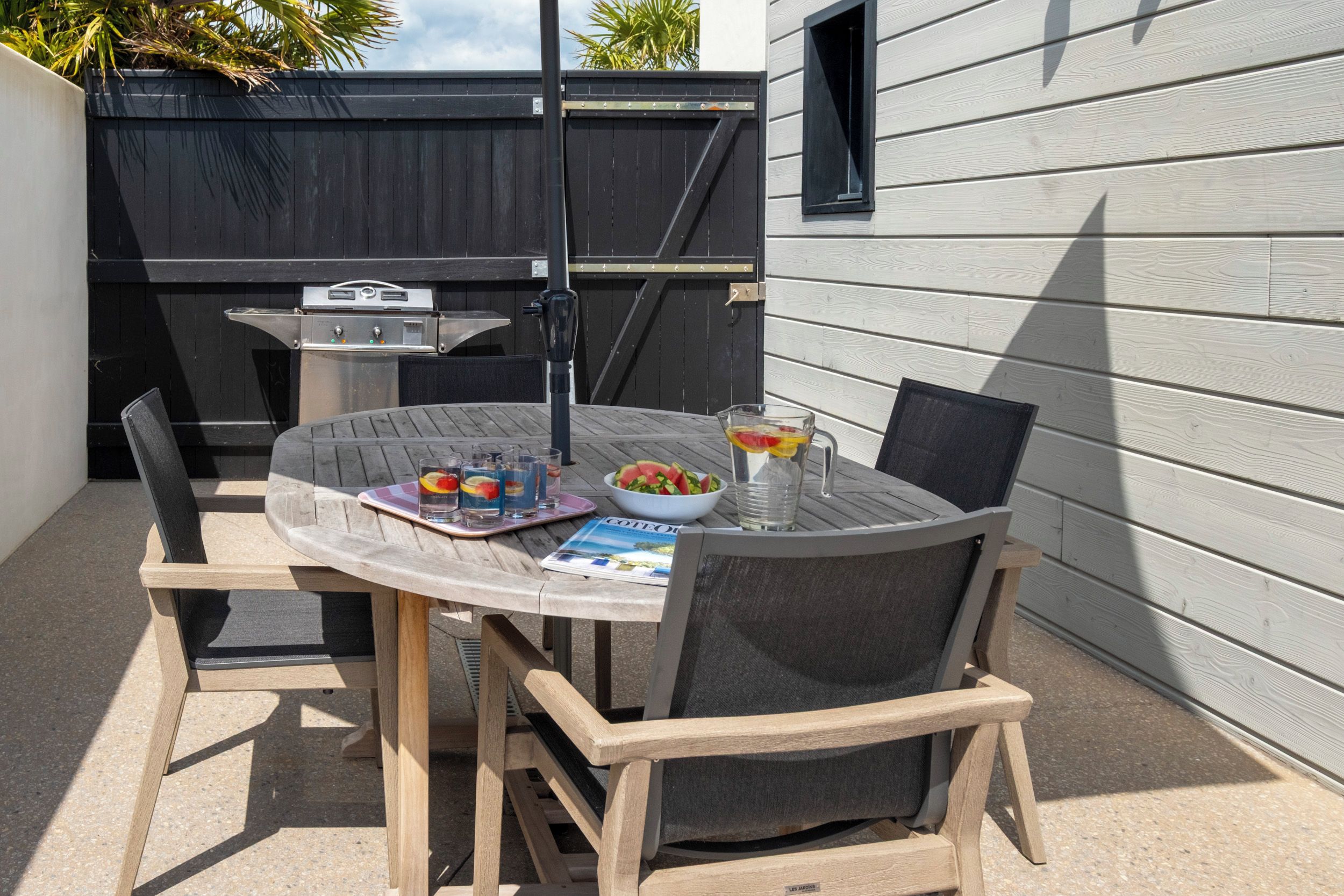 A round wooden table with chairs, a grill, and a bowl of salad.