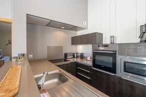 A modern kitchen with dark cabinetry, stainless steel appliances, and a built-in oven. - Mv Lodge (La Couarde-sur-Mer)