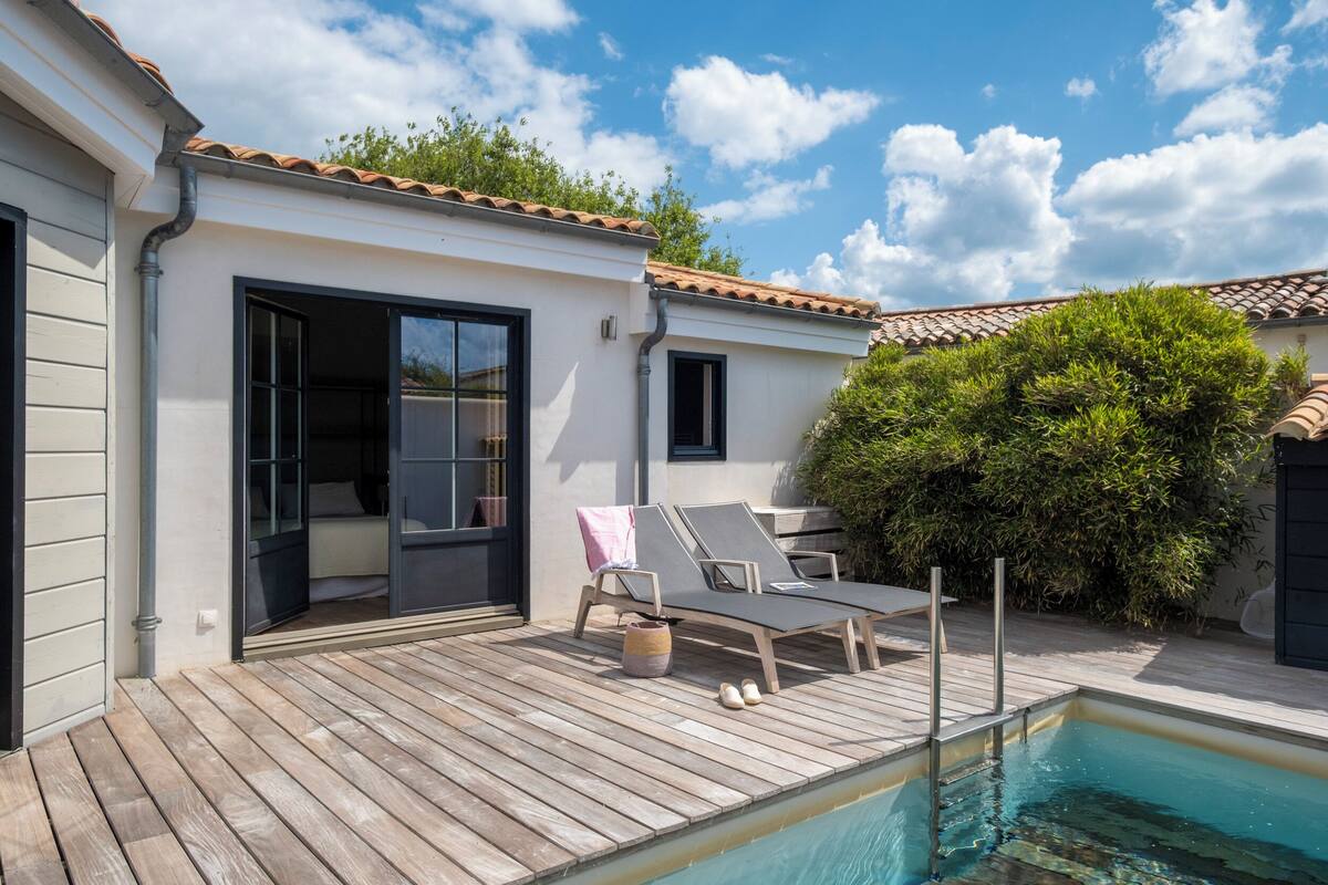 Un espace aménagé au bord de la piscine, avec une terrasse en bois, une petite piscine et deux chaises longues.