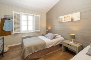 A bedroom with a bed, nightstands, a window with shutters, a radiator, a wall-mounted artwork, and a hanging garment rack. - Mv Lodge (La Couarde-sur-Mer)