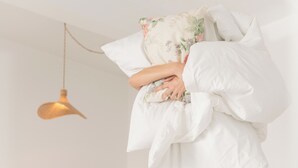 Eine Person steht auf einem Bett in einem Zimmer mit einer Couch, einem Tisch und einer Hängelampe.