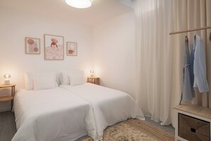 A bedroom with two beds, a nightstand with a lamp, a wardrobe, and three wall-mounted artworks.