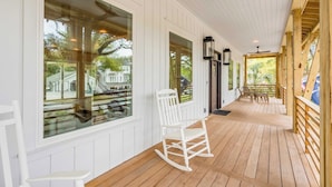 A wooden deck with a rocking chair and a table, large windows, and a ceiling fan.