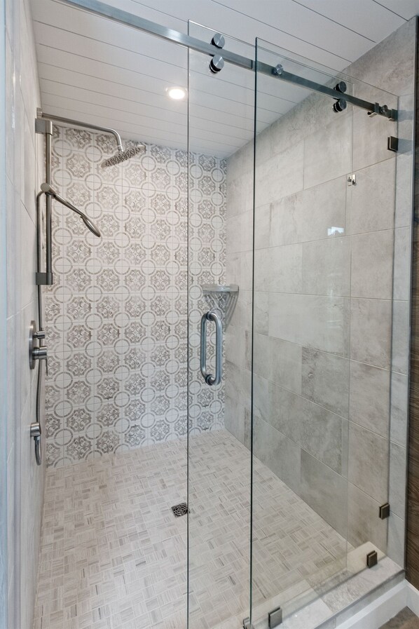 A glass-enclosed shower with a patterned tile wall and a metal showerhead.