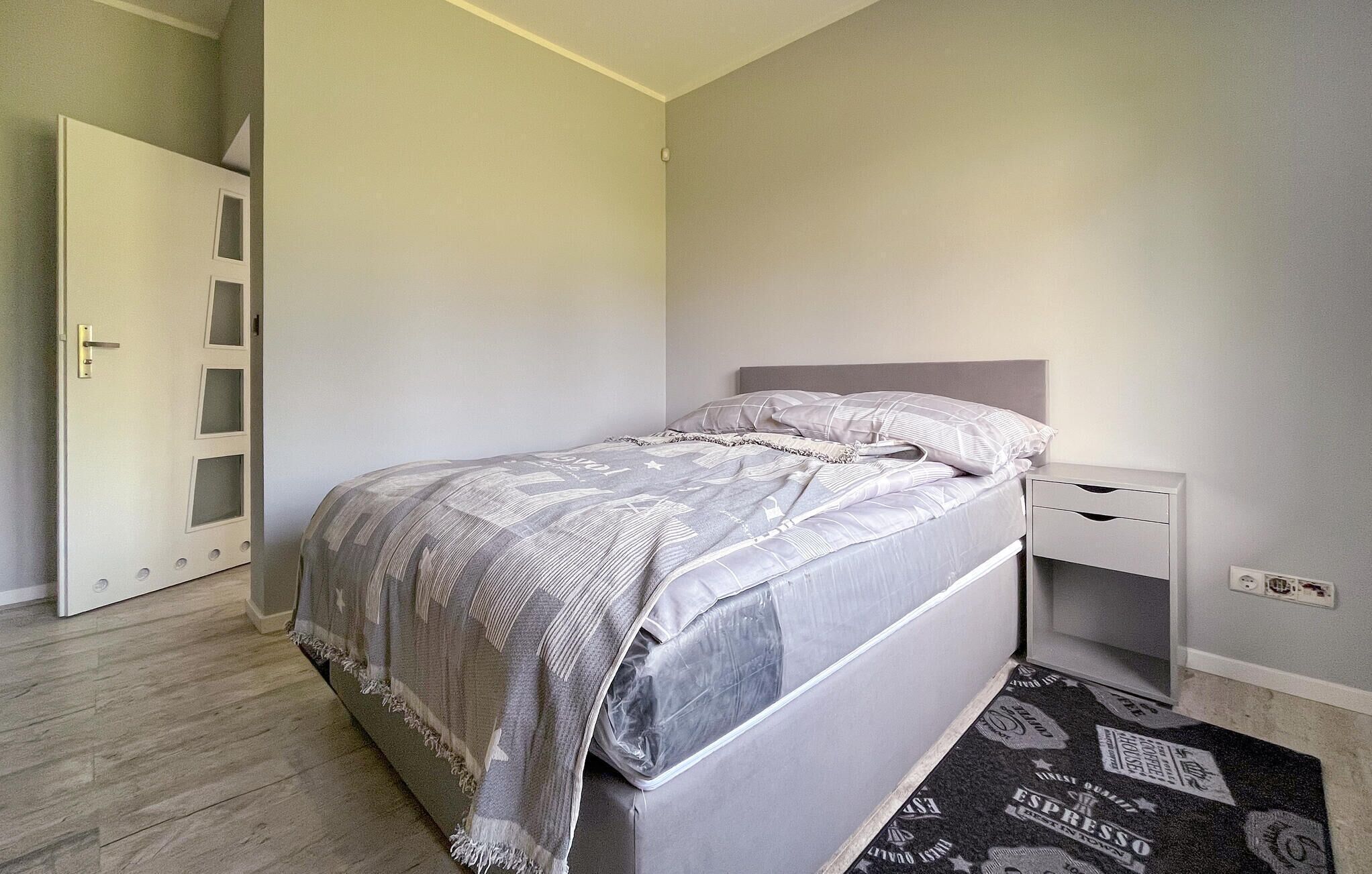 Un dormitorio con cama, mesita de noche y puerta con paneles de vidrio esmerilado.