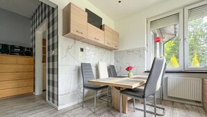 Eine moderne Küche mit Essbereich, ausgestattet mit einer Marmor-Spritzschutzleiste, Holzschränken und Blick auf Bäume durch das Fenster.