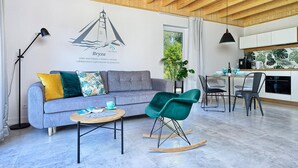 A modern living room with a grey sofa, teal rocking chair, and a small wooden table. A mural of a lighthouse is on the wall, and there's a kitchen area in the background. - Lovely home in Bialogora with WiFi (Bialogora)