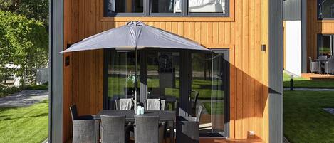 A modern outdoor dining area with a table and chairs, a large umbrella, and a glass enclosure.