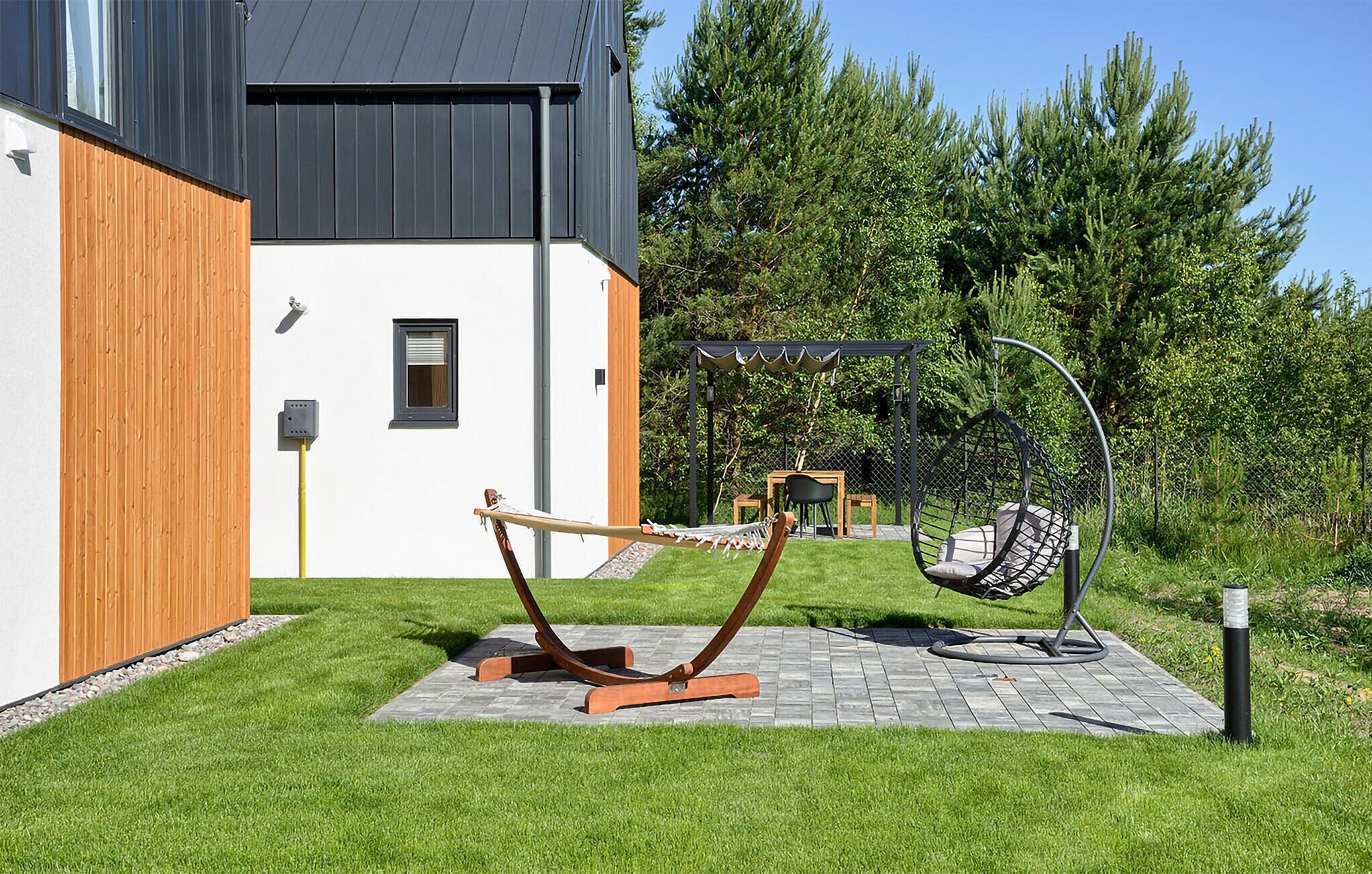 A modern house with a wooden fence, a hammock, and a swing set in the garden.