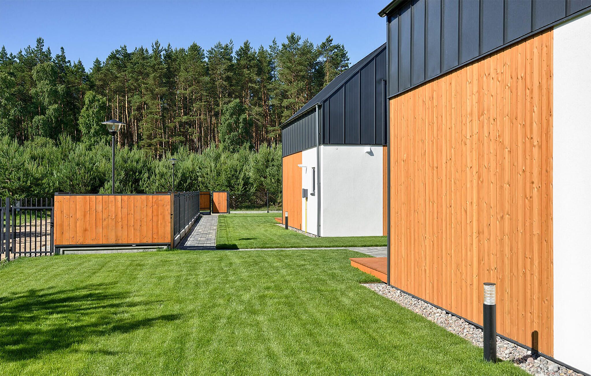 Un bâtiment moderne dont les murs extérieurs sont un mélange de bois et de métal, avec une pelouse bien entretenue et un paysage boisé en arrière-plan.