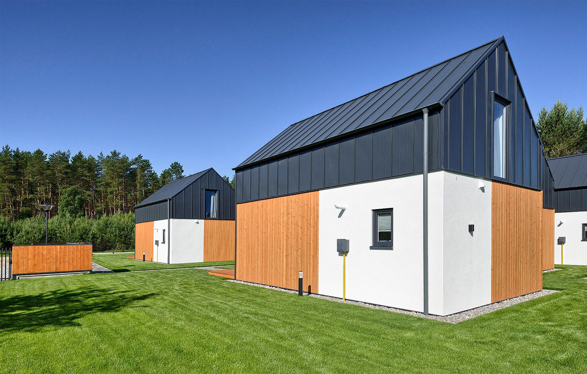 A modern residential building with a sloped roof, large windows, and a combination of white and wooden exterior walls.