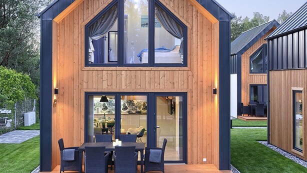 Una casa moderna de dos pisos con fachada de madera, amplios ventanales y una terraza con mobiliario exterior.