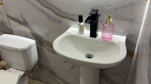A bathroom with a white sink, a black faucet, and a pink bottle of hand soap.