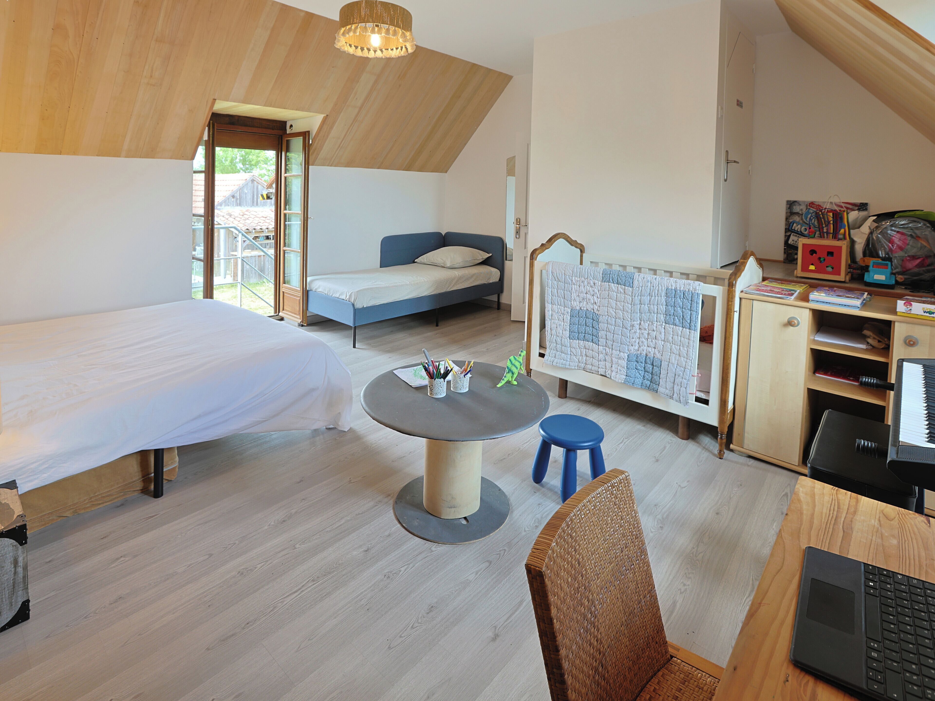 A modern bedroom with a lofted sleeping area, a round table with a chair, and a desk with a laptop.