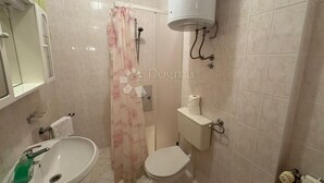 A bathroom with a toilet, sink, shower curtain, and a water heater mounted on the wall. - Vila with 25 rooms (Dramalj)