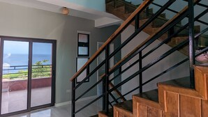 Una escalera moderna con escalones de madera y barandillas negras, que lleva a un balcón con vistas al océano.