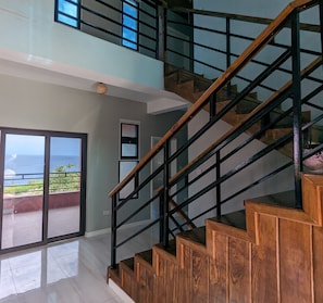 A modern staircase with wooden steps and black railings, leading to a balcony with a view of the ocean. - Exquisite Sunset Vista home in Mero (Mero)