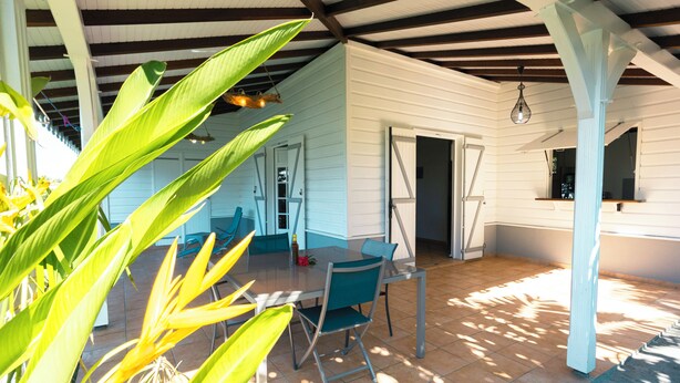 A covered patio area with a table and chairs, a door leading to an interior space, and a hanging light fixture.