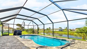 A covered swimming pool with a view of a lake and houses in the background.