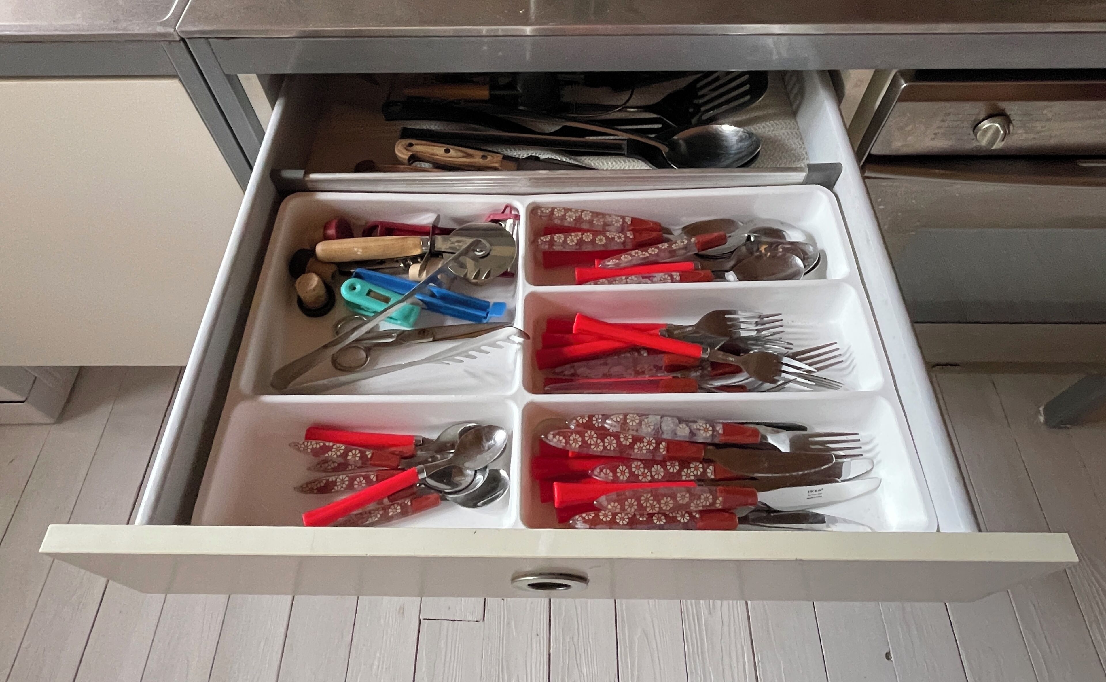 Un cajón con divisiones que contiene diversos utensilios de cocina.