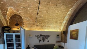 Un vaste espace de vie doté d’un plafond en briques, d’un canapé gris, d’une armoire blanche et d’une table à manger agrémentée d’un saladier.