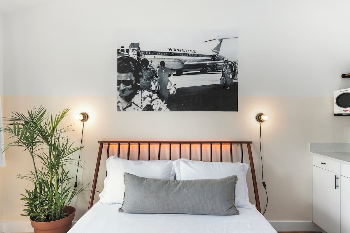Una camera da letto con un letto, una pianta in vaso, un lampadario a parete e un poster di un aereo hawaiano.