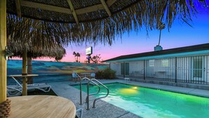A pool area with a thatched roof, lounge chairs, and a sign indicating 'Aloha'. - Aloha Breeze (Chandler)