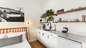 A modern hotel room with a bed, a kitchenette, and a wall-mounted shelf with kitchen items. - Aloha Breeze (Chandler)