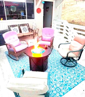 Un espacio al aire libre con sillas de mimbre, una mesa redonda, una cerca blanca y un tapete azul con estampado.