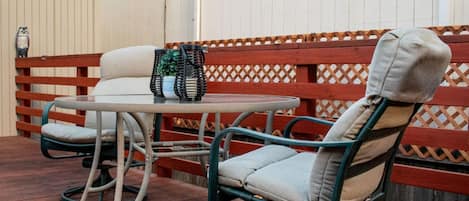 Une terrasse avec une table ronde et deux chaises, une clôture en bois et une petite décoration représentant une chouette.