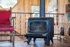 A wooden cabin interior with a wood-burning stove, a red chair, and a glass table with candles.