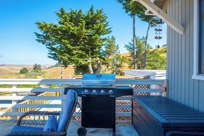 Un barbecue installé sur une terrasse, avec vue sur un arbre et des collines.