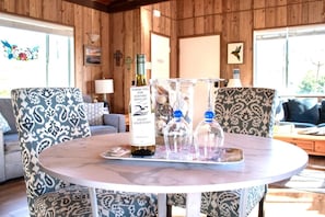 A round table with a bottle of wine, two glass bottles, and a tray in a room with patterned chairs and wooden walls.