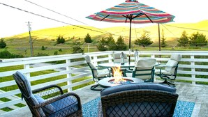Une terrasse extérieure aménagée avec des meubles en osier, un foyer et un parasol coloré.