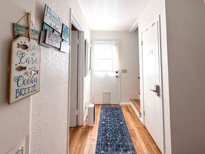 A hallway with a wooden floor, a blue patterned rug, and a white door at the end.