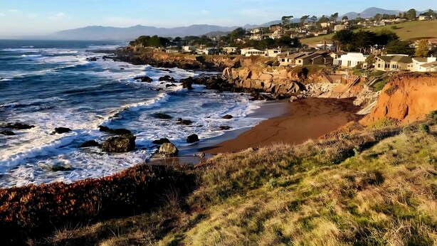 Une ville côtière avec un littoral rocheux, des vagues qui s’écrasent sur la plage et des maisons construites le long de la falaise.