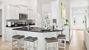 A modern kitchen with white cabinetry, a black countertop, and a central island with stools. - Newley Built/Heated Pool/Golf Course Views/Sleeps 9 (Rotonda West)