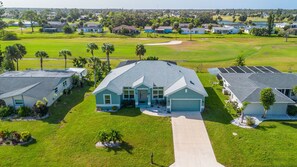 Un quartier résidentiel avec une maison principale dotée d’un grand garage, entourée de maisons plus petites et avec un terrain de golf en arrière-plan.