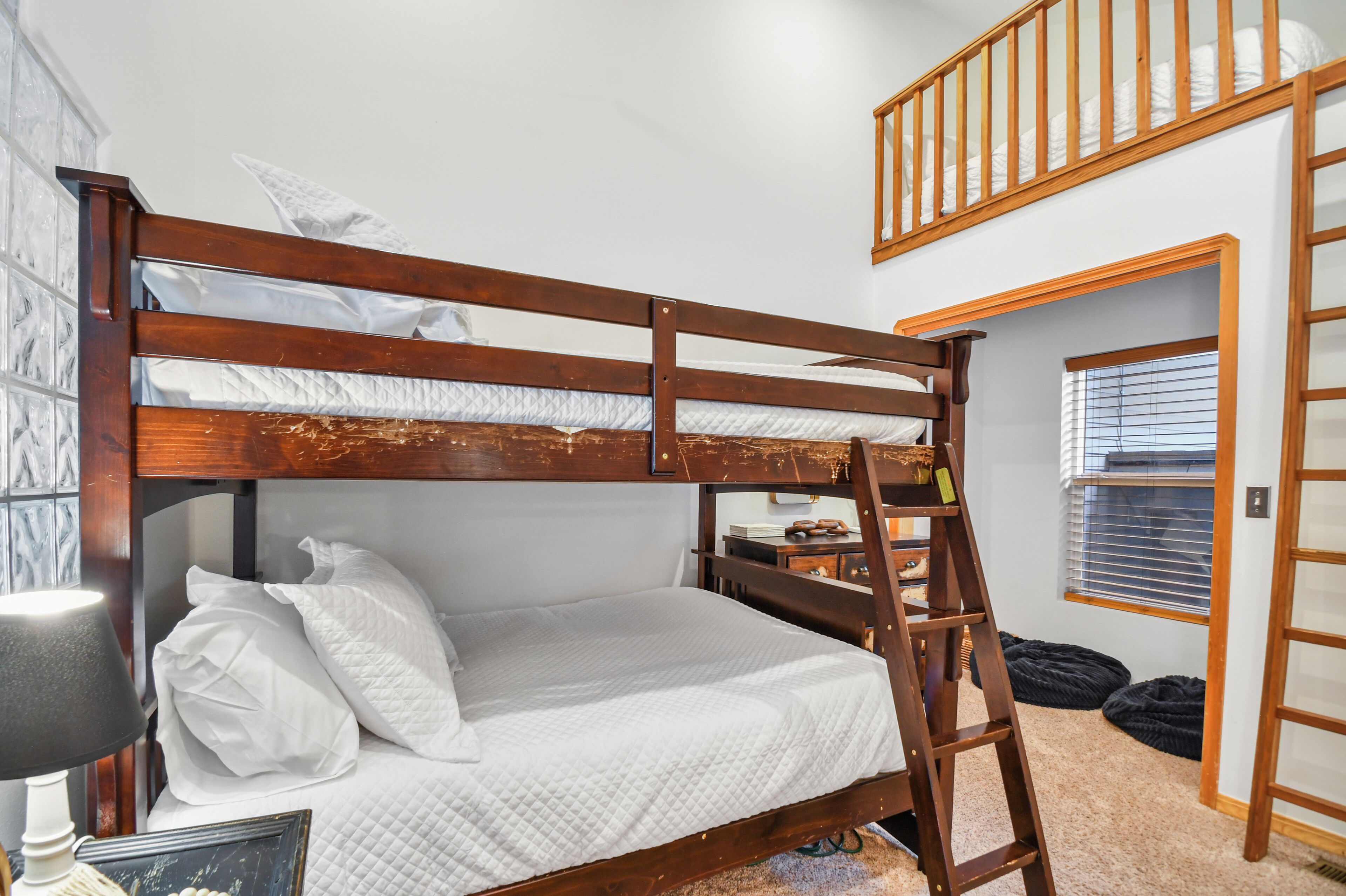 A bunk bed with a wooden ladder, white bedding, a bedside lamp, and a small bedside table with a picture frame.