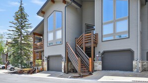 A two-story building with a modern design, featuring a staircase with wooden railings leading to a second-floor entrance, and a garage with a stone base. - Deer Valley La Casa Boulder Creek (Park City)